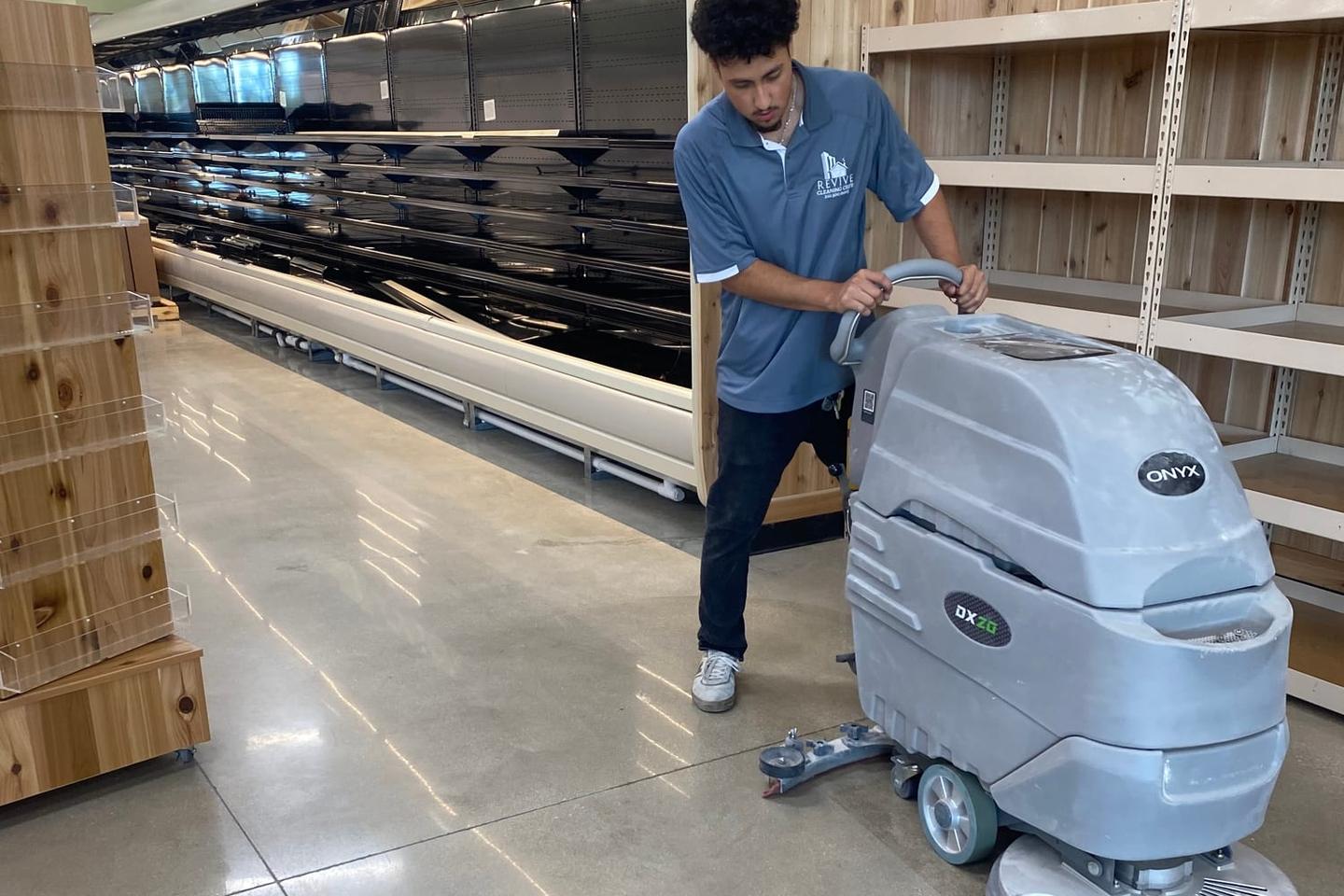 A Revive Cleaning Crew technician running a walk-behind floor scrubber across a polished concrete floor on a San Antonio job