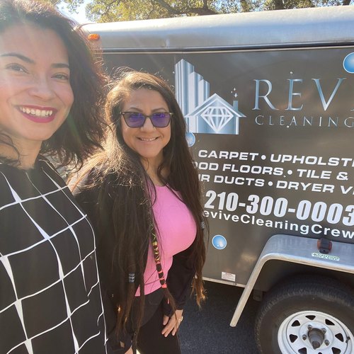 Two members of the Revive Cleaning Crew team standing beside the company's branded equipment trailer